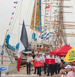 A crowd at Harbor Fest with a tall ship in the background