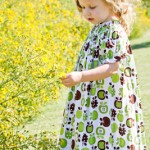 Mackenzie (2) wears a fall print dress of green and brown apples while checking out the landscape. The outfit provided by The Ragamuffin Shop is paired with a green hair bow.