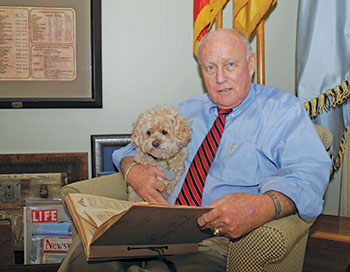 Pat Waters and his dog Max look over press clippings about Pat’s iconic relative. He keeps the scrapbook in a room in his Mount Pleasant home that is dedicated to his famous grandfather.