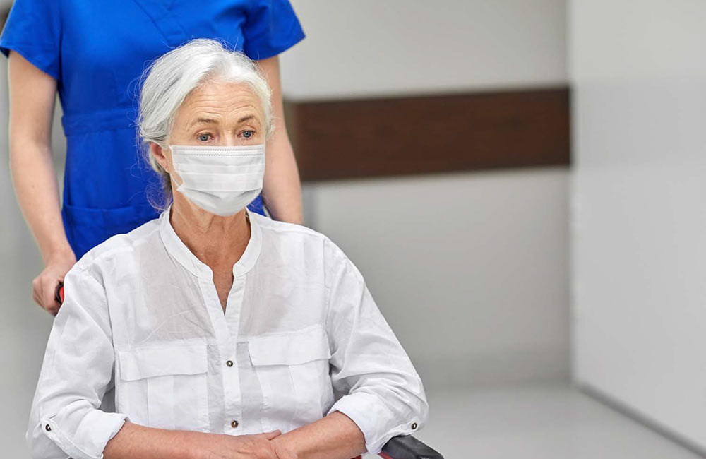 Photo of a woman at the hospital in a wheelchair wearing a mask for the Locals Overcome the COVID-19 Virus article