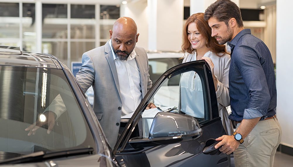 An auto sales manager showing a vehicle to a couple.