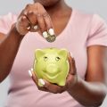 A woman puts a coin into her piggy bank for savings.
