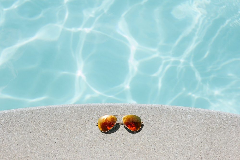 Photo of a swimming pool with sunglasses on the side. (photo by Pexels from Pixabay)