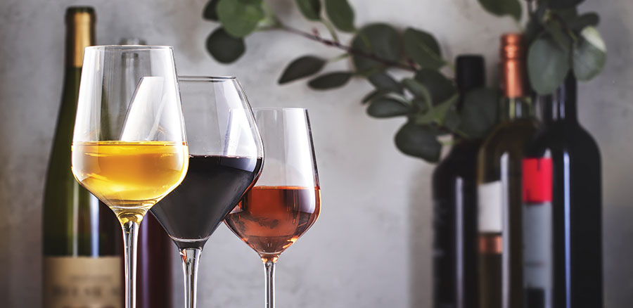 White, red and rose wine in wine glasses with bottles of wine in the background.