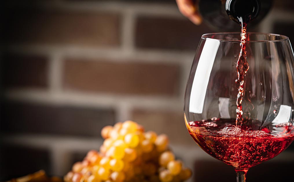 Pouring red wine into a glass with grapes in the background.