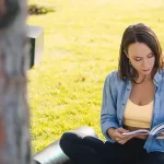A woman enjoying reading a book under a tree