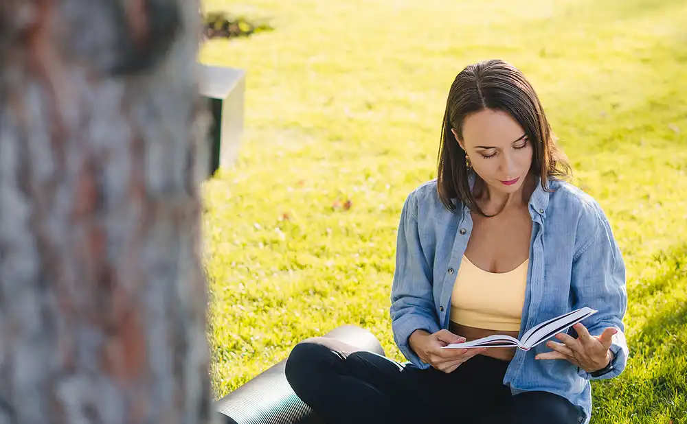 A woman enjoying reading a book under a tree