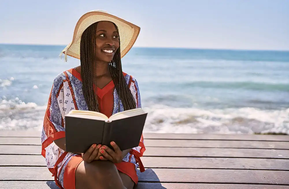 A young woman reading a book at the beach.