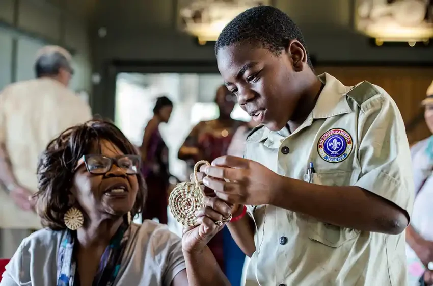 Henrietta Snype, a master sweetgrass basket maker, shows a young boy scout how to start a small basket.