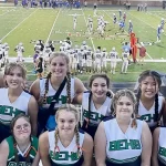 Cheerleaders with a football game in the background.