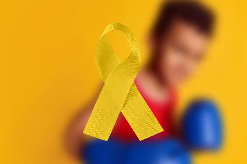 Childhood cancer Awareness graphic: blurry photo of a young boy with boxing gloves and a yellow ribbon in the forefront
