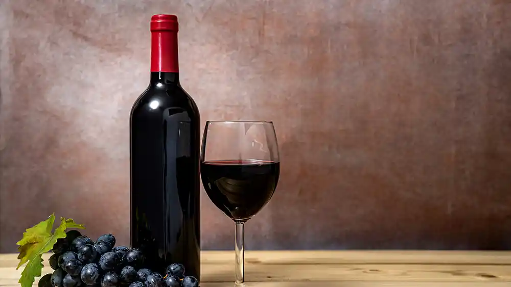 A bottle of wine, and a glass of wine pictured with grapes.