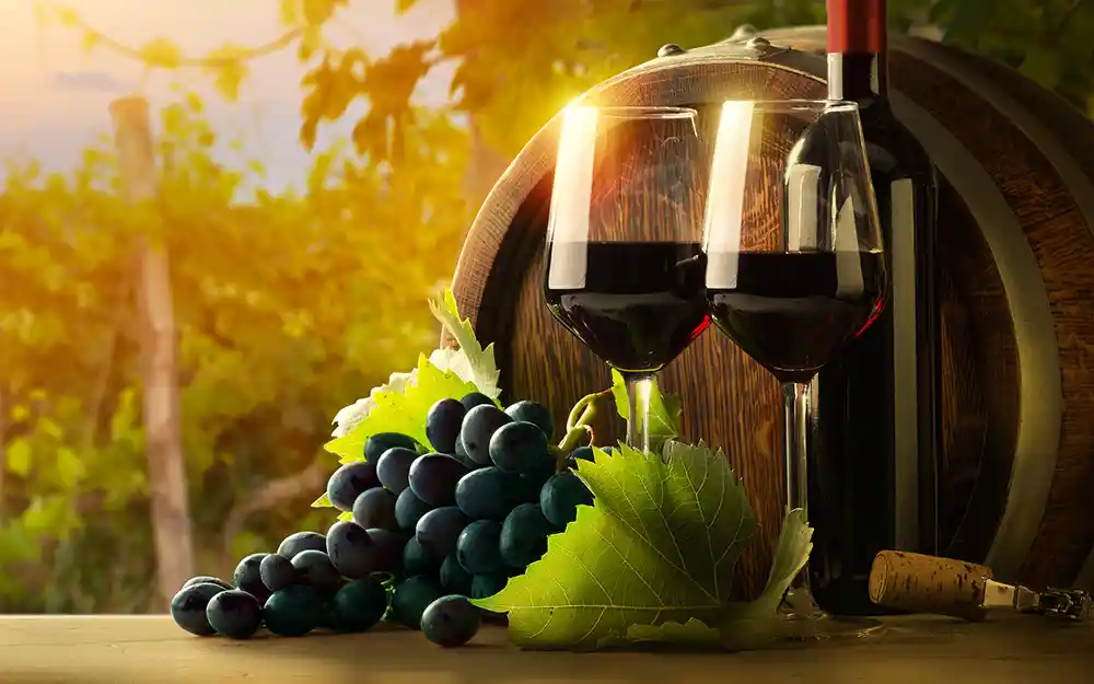 Glasses of red wine, a bottle of wine, grapes and a wine barrel