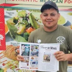 Cachita’s Kitchen Owner Jose Cruz in front of his food truck holding a copy of his article in Mount Pleasant Magazine.