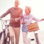 Active senior couple walking bikes on the beach