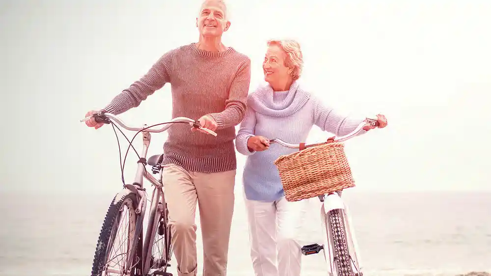 Active senior couple walking bikes on the beach