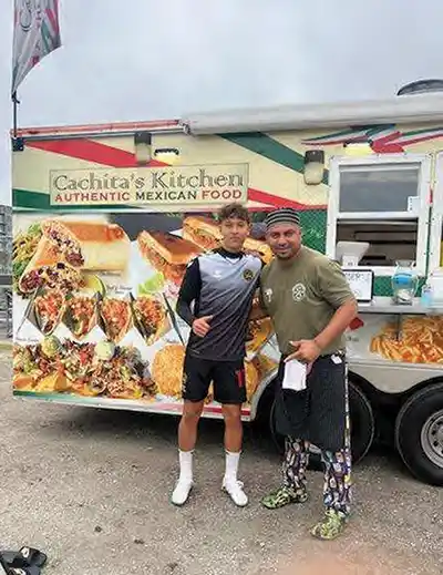 Cachita’s Kitchen Owner Jose Cruz (right) poses in front of his food truck at a Charleston Battery game with former player and friend Fidel Barajas.