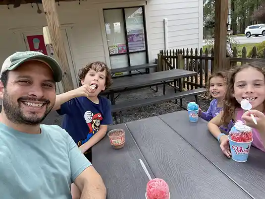 Photo of Ethan Levy and his three oldest children enjoying shaved ice treats from Pelican’s SnoBalls.