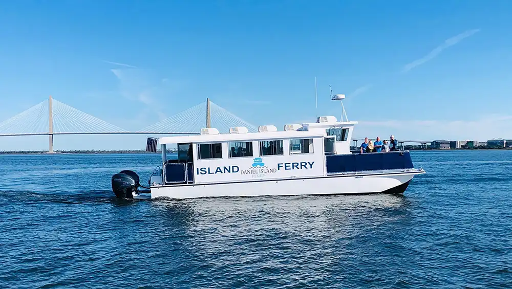 A Daniel Island Ferry moving across Charleston Harbor with the Ravenel Bridge in the background.