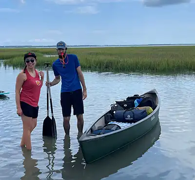 Capers Island campers Savannah and Geoff standing next to a canoe with an emergency whistle.