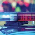 The roof of a police cruiser with lightbar turned on with a blurred crowd in the background.