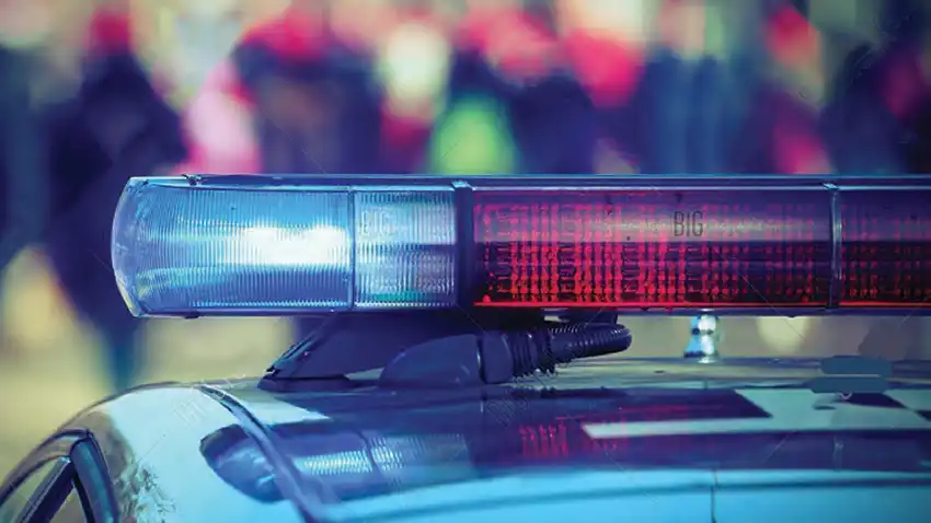 The roof of a police cruiser with lightbar turned on with a blurred crowd in the background.