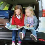 2 young girls sitting in the back of an SUV while it's getting packed.