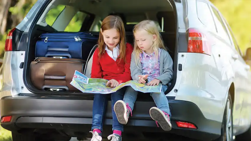 2 young girls sitting in the back of an SUV while it's getting packed.