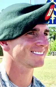 A photo from the side of CPT Richard “Richie” G. Cliff, Jr. smiling, wearing his green beret bearing Captain's bars, his rank insignia.