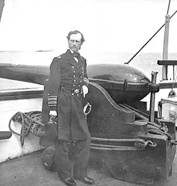 Admiral Dahlgren stands aboard a ship near a cannon.