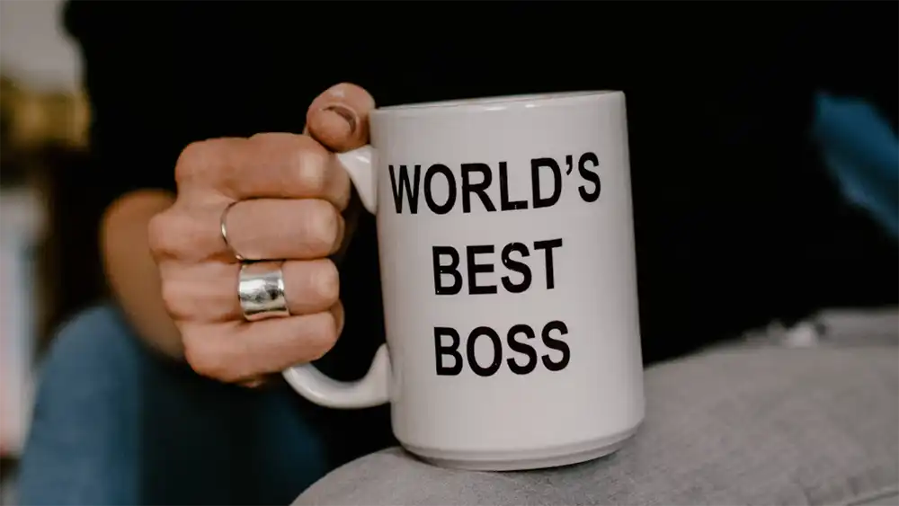 A woman holidng a World's Best Boss coffee mug. (Edited) photo by Kelly Sikkema on Unsplash.