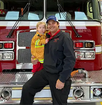 Paul Sottile giving 2-year-old son Silas an up-close view of a fire engine and miniature uniform.