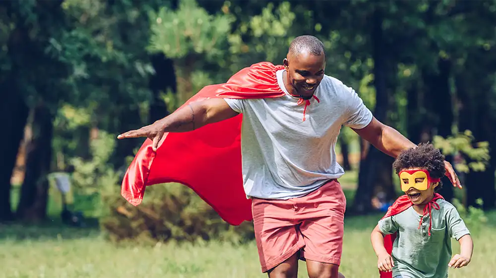 Superhero dad with his superhero son running in their yard.