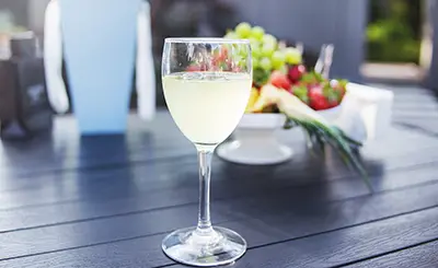 A glass of wine on a table with fruit in the background