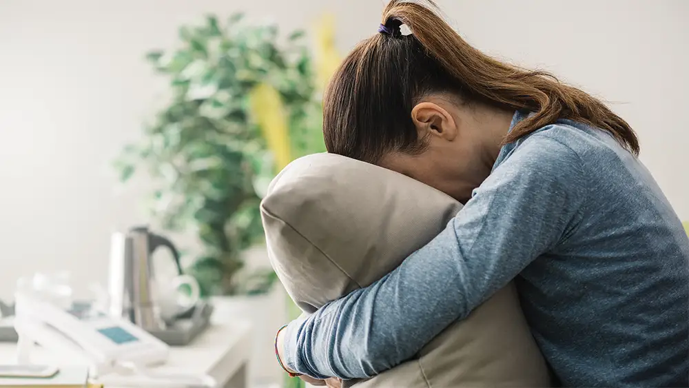 A woman with SAD feeling depressed cries into a pillow