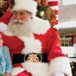 A little girl sits next to Santa and tells him what she wants for Christmas.