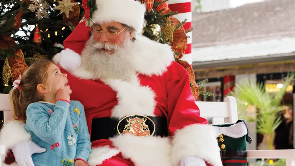 A little girl sits next to Santa and tells him what she wants for Christmas.