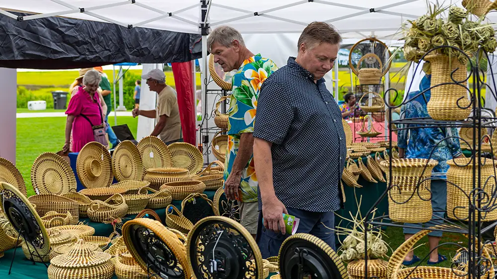An outdoor festival booth filled with dozens of detailed, hand-woven sweetgrass baskets on display at the Mount Pleasant Sweetgrass Festival.
