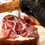 βSuch a Nice Italian Boyβ artisan sandwich being fresh-made at The Pass Panino and Provisions with hot and sweet soppressata, mortadella, burrata, greens, red onion, tomato, housemade Italian vinaigrette, sharp provolone and pickled Calabrian chili relish on ciabatta.